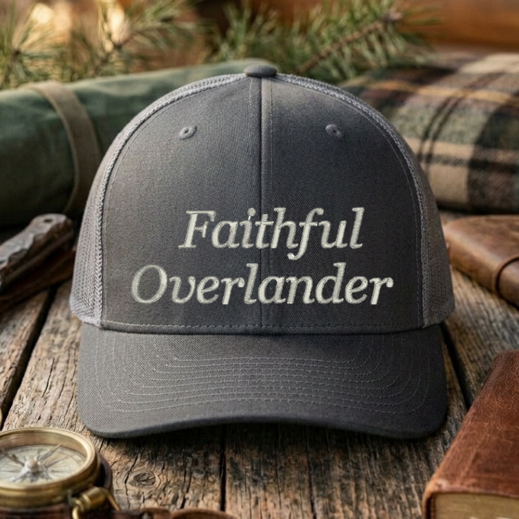 Gray cap with 'Faithful Overlander' text on a wooden surface with outdoor gear.