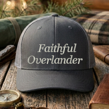Gray cap with 'Faithful Overlander' text on a wooden surface with outdoor gear.