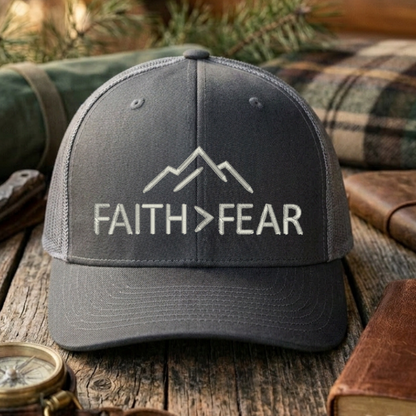 Gray cap with 'FAITH > FEAR' text on a wooden surface with outdoor items.