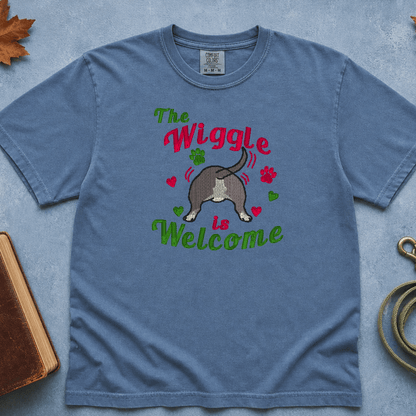 Woman wearing blue jean Comfort Colors tee with embroidered 'The Wiggle is Welcome' bully breed design, standing outdoors with a blue nose pit bull