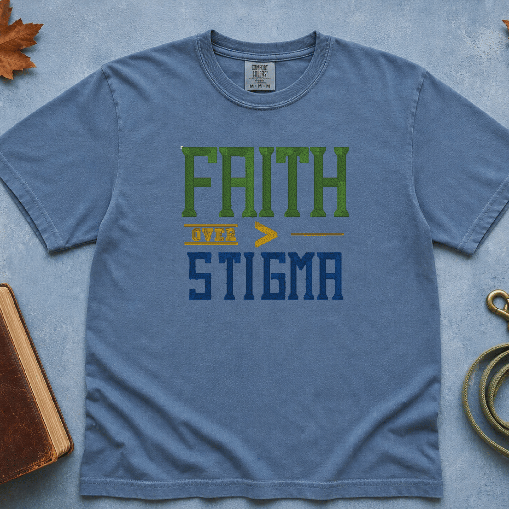 Faith Over Stigma Comfort Colors Tee in Blue Jean flatlay with Holy Bible and dog leash on blue background with autumn leaves