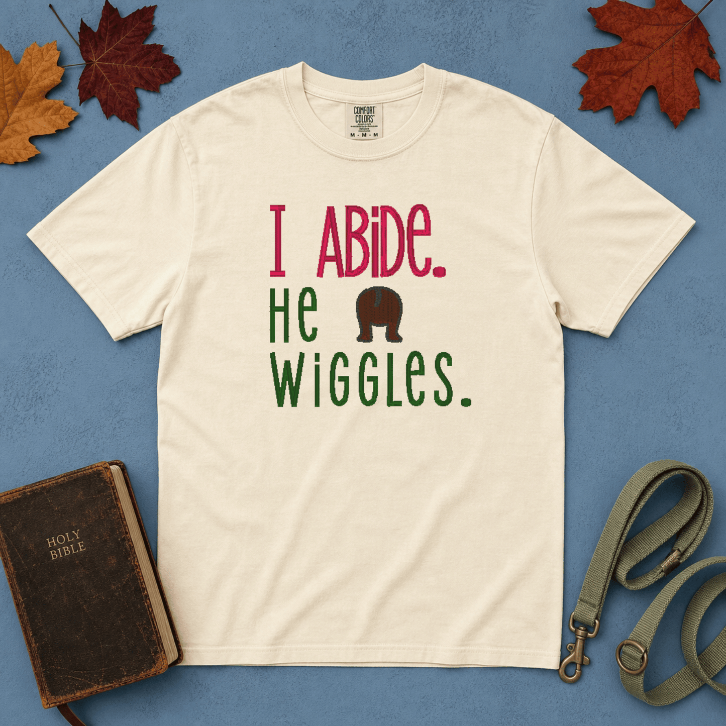 I Abide He Wiggles Comfort Colors Tee in Ivory flatlay with Holy Bible and dog leash