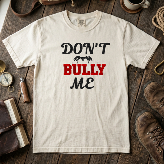 White t-shirt with 'Don't Bully Me' text on a wooden surface with rustic items.