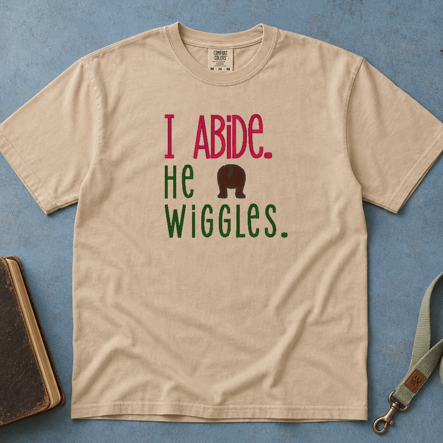 I Abide He Wiggles Comfort Colors Tee in Sandstone flatlay with Holy Bible and dog leash