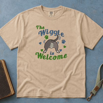Sandstone Comfort Colors tee with embroidered 'The Wiggle is Welcome' bully breed design, lifestyle photo with woman holding coffee mug and pit bull beside her