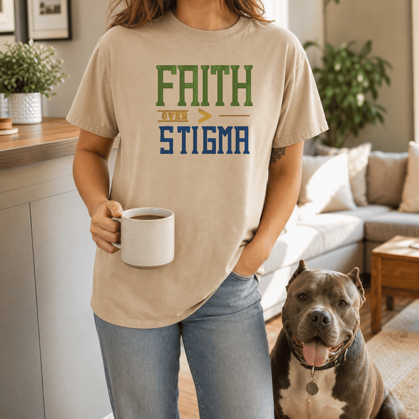 Woman wearing Faith Over Stigma tee in Sandstone holding coffee mug standing with grey bully breed dog