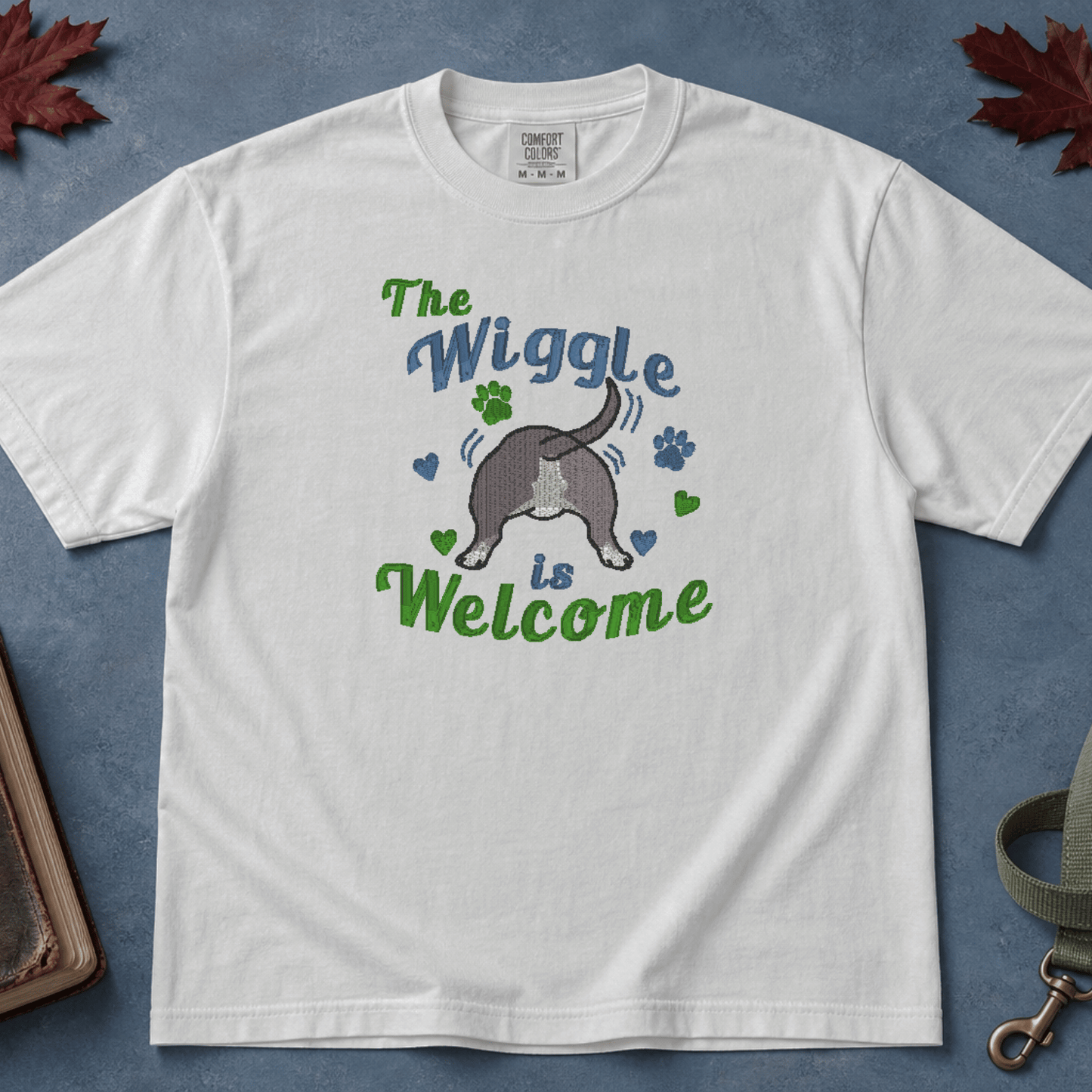 White Comfort Colors tee with embroidered wiggle butt bully breed design, flatlay on blue background with Bible and leash — Abiding Paws