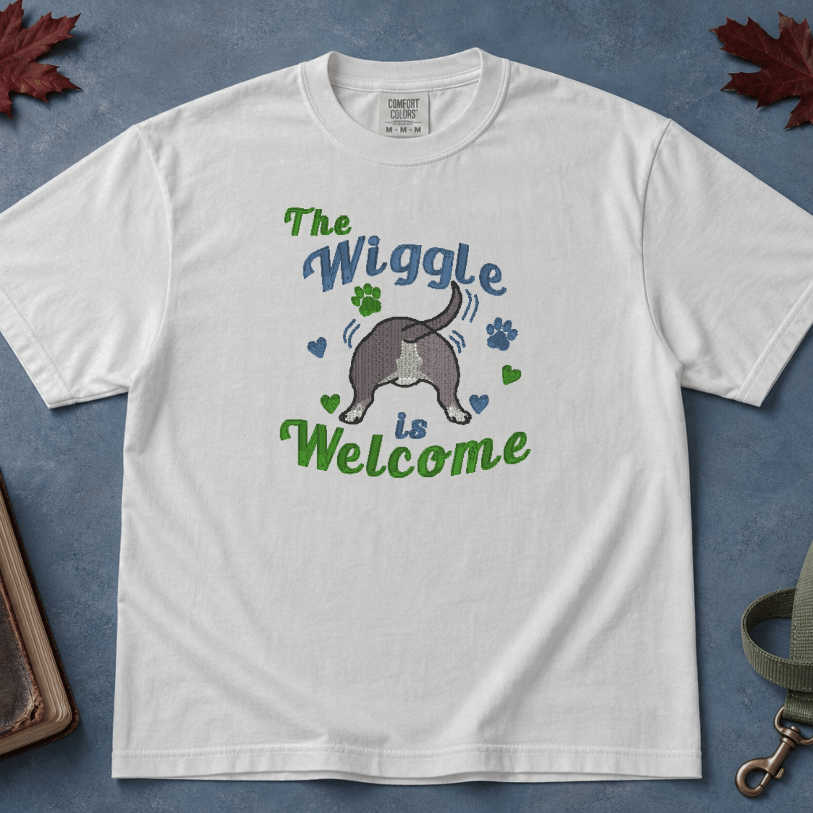 White Comfort Colors tee with embroidered wiggle butt bully breed design, flatlay on blue background with Bible and leash — Abiding Paws