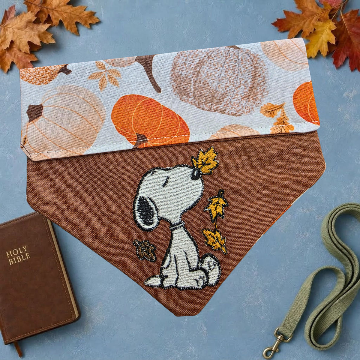 Brown dog bandana with embroidered white dog and autumn leaves, folded to show pumpkin-print reverse