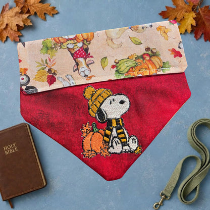 Red dog bandana embroidered with a white pup in golden hat and scarf beside a pumpkin